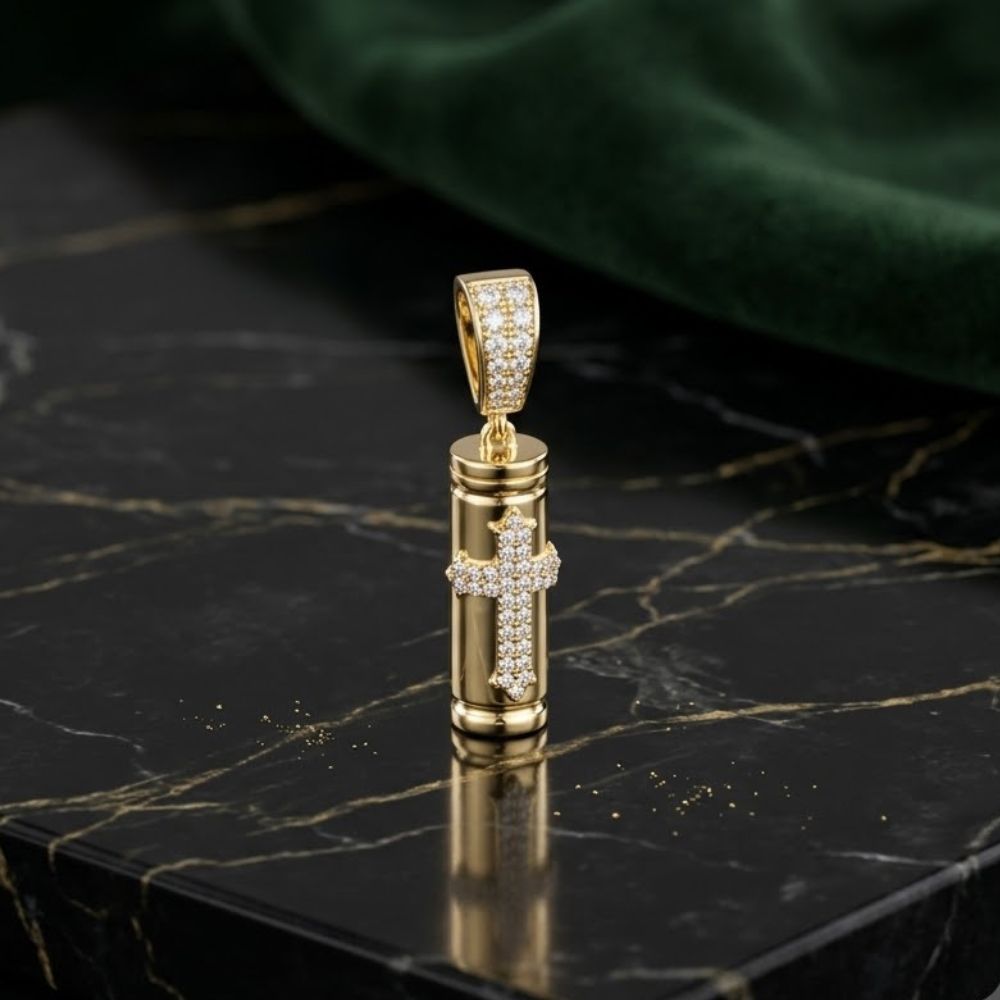 The Diamond Urn Charm 3/8CT 10K Gold Pendant is a men's remembrance piece with a diamond-studded cross cylinder, displayed on black marble accented by white veins and set against a green fabric backdrop.