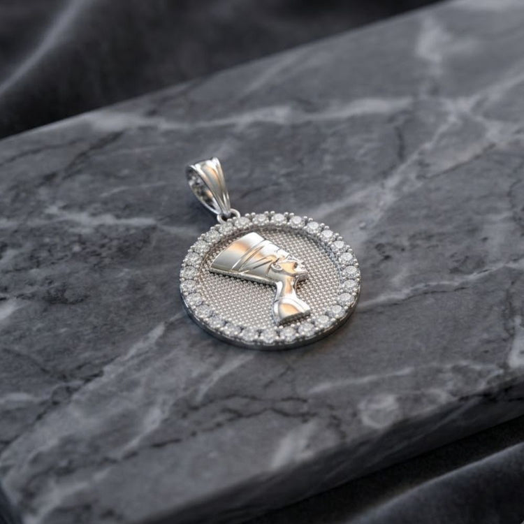 The Sterling Silver CZ Nefertiti Egyptian Pendant, featuring the profile of an Egyptian queen encircled by sparkling cubic zirconia gemstones, rests on a dark gray marble surface.