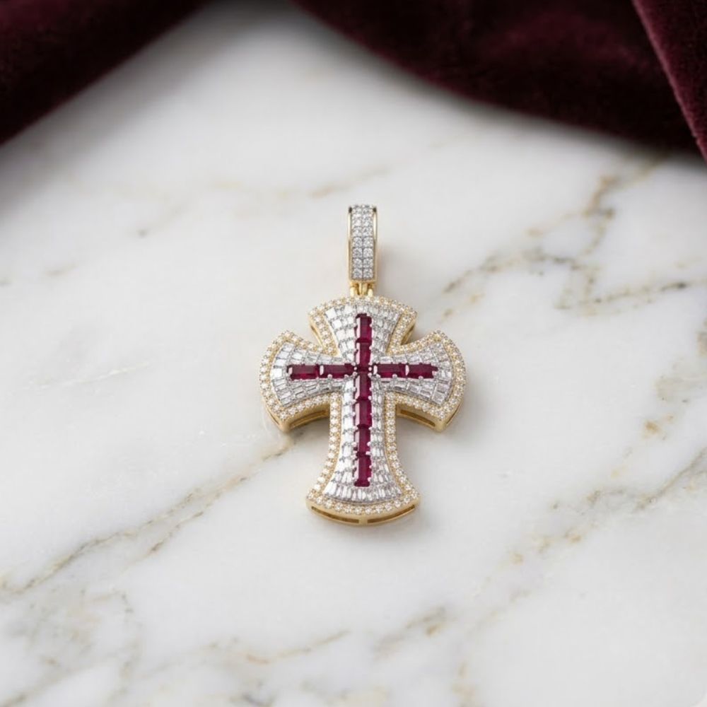 The Diamond Ruby Cross Charm 1CTW 10K Gold features small white diamonds and a central baguette ruby cross design, displayed on white marble with a dark red velvet cloth nearby.