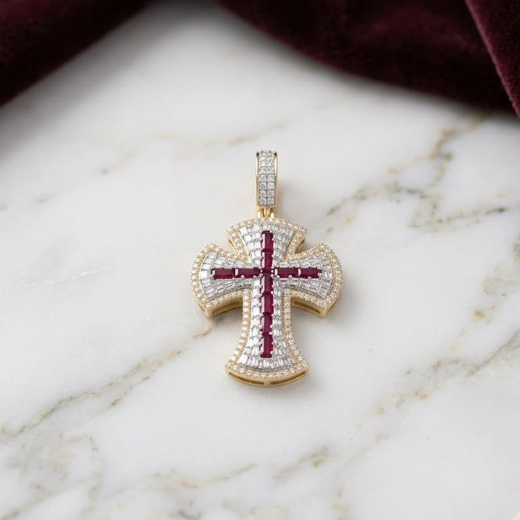 The Diamond Ruby Cross Charm 1CTW 10K Gold features small white diamonds and a central baguette ruby cross design, displayed on white marble with a dark red velvet cloth nearby.