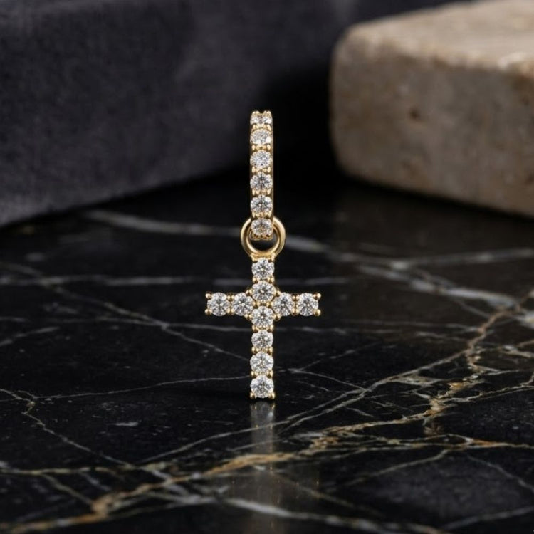 The 14K Yellow Gold 1/5 CTW Diamond Cross Pendant is displayed on a black marble surface, with light-colored stone blocks in the background.