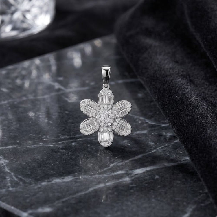 The 14K White Gold Diamond Flower Pendant 1/2 CTW, featuring an elegant five-petal design, is displayed atop a polished black marble surface, with gentle black fabric draped nearby and a faceted glass object in the background.