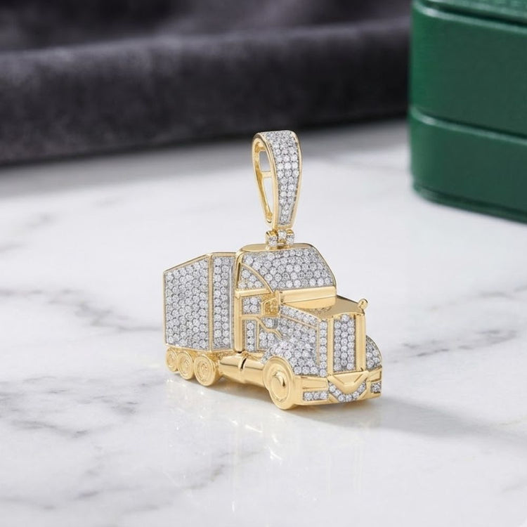 The Sterling Silver Diamond Truck Charm 7/8CTW, a striking men’s pendant shaped like a semi-truck and encrusted with diamonds, is displayed on a marble surface with a blurred green box and grey cloth in the background.