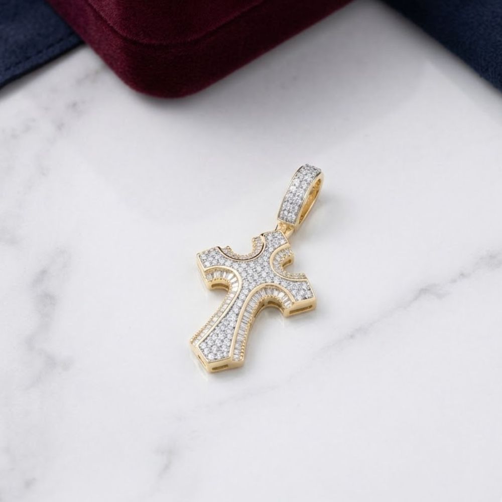 The Diamond Cross Charm 5/8CT 10K Yellow Gold rests on a white marble surface, accented by glimpses of dark blue and burgundy fabric in the corners.