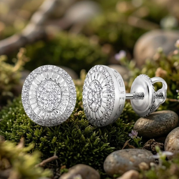 Close-up of the Sterling Silver Round Diamond Oval Earrings 1/3 Cttw, featuring intricate detailing and sparkling diamonds, displayed on green moss and surrounded by smooth stones outdoors.