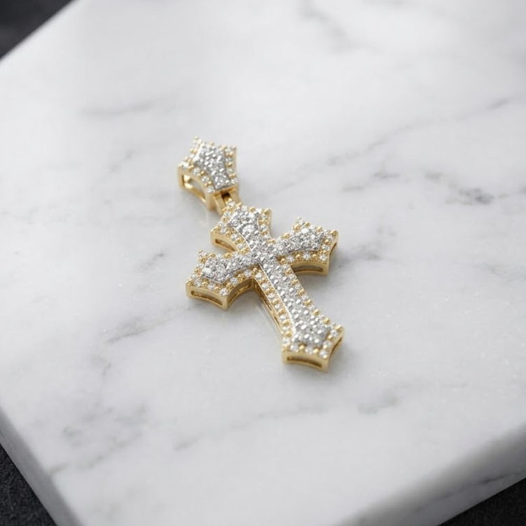 A 1/4 CTW Natural Diamond Cross Pendant in 10K gold, adorned with sparkling diamonds, rests elegantly on a white marble surface.