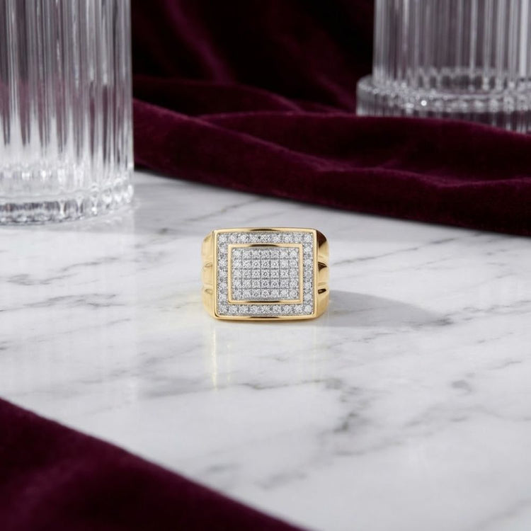 A 10k Yellow Gold Diamond Square Ring 1/2 CT rests on a white marble surface, framed by rich burgundy fabric and glass columns in the background.