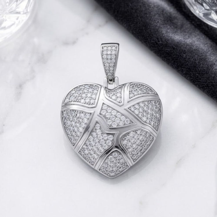 The 925 Sterling Silver Women’s CZ Heart Charm Pendant features a heart-shaped design adorned with sparkling cubic zirconia and a distinctive geometric, cracked pattern. This elegant pendant, crafted from high-quality 925 sterling silver, rests gracefully on a white marble surface beside a dark fabric, showcasing both modern sophistication and timeless beauty.