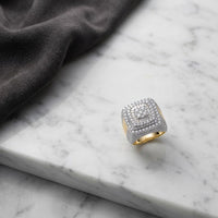 A striking 10K Yellow Gold Baguette Diamond Cluster Ring, adorned with sparkling diamonds in a square formation, rests on a marble surface beside folded dark fabric. This elegant piece effortlessly blends sophistication and style with its timeless yellow gold setting and radiant diamond cluster design.