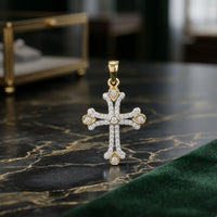 The 1/4CTW Diamond Cross Pendant in 10K Yellow Gold rests on a dark marble surface, its sparkling diamonds and gold accents shining, while a blurred jewelry box sits in the background.