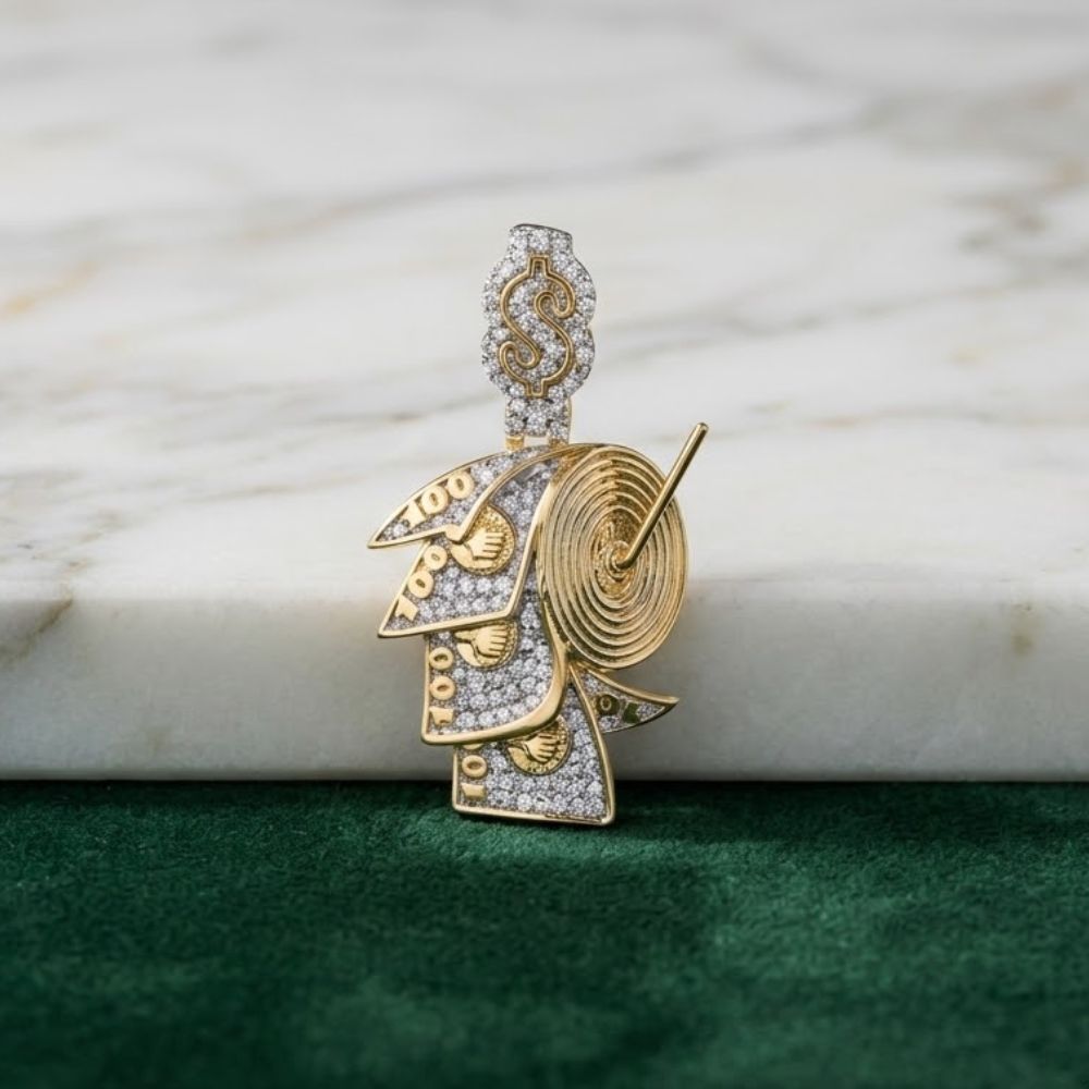 The 10K Gold Diamond Money Roll Charm 1/4CTW features a rolled $100 bill design with a diamond-studded dollar sign on top, displayed on marble above a green textured surface.