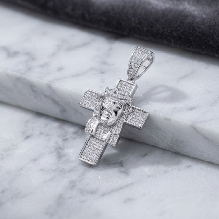 Sterling Silver Moissanite Jesus Cross Pendant featuring a detailed face adorned with a crown of thorns and set with sparkling moissanite-like stones, elegantly displayed on a white marble surface—an eye-catching religious charm for any collection.