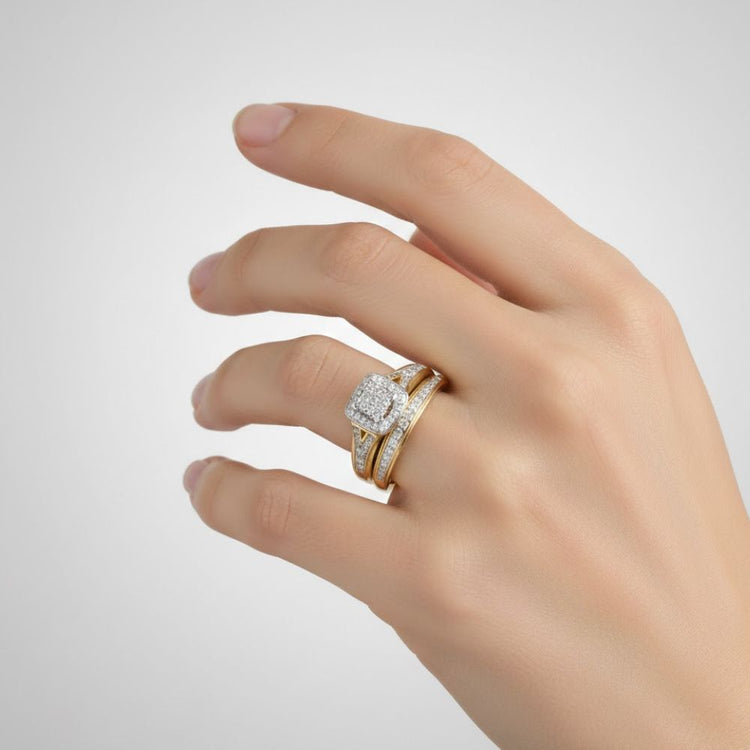 A hand with neatly manicured nails wears the 3/4 CTW 10k Yellow Gold Wedding Trio Set, showcasing a princess style diamond ring with a square-shaped center stone and a matching band on the ring finger.