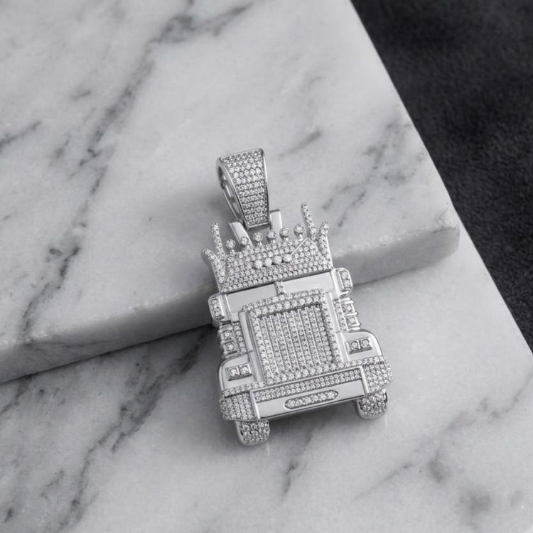 A 1-1/3CTW Diamond Truck Charm in sterling silver, shaped like a crowned truck and resting on a white marble surface against a dark textured background, exemplifies the bold allure of men’s jewelry and the brilliance of natural diamonds.