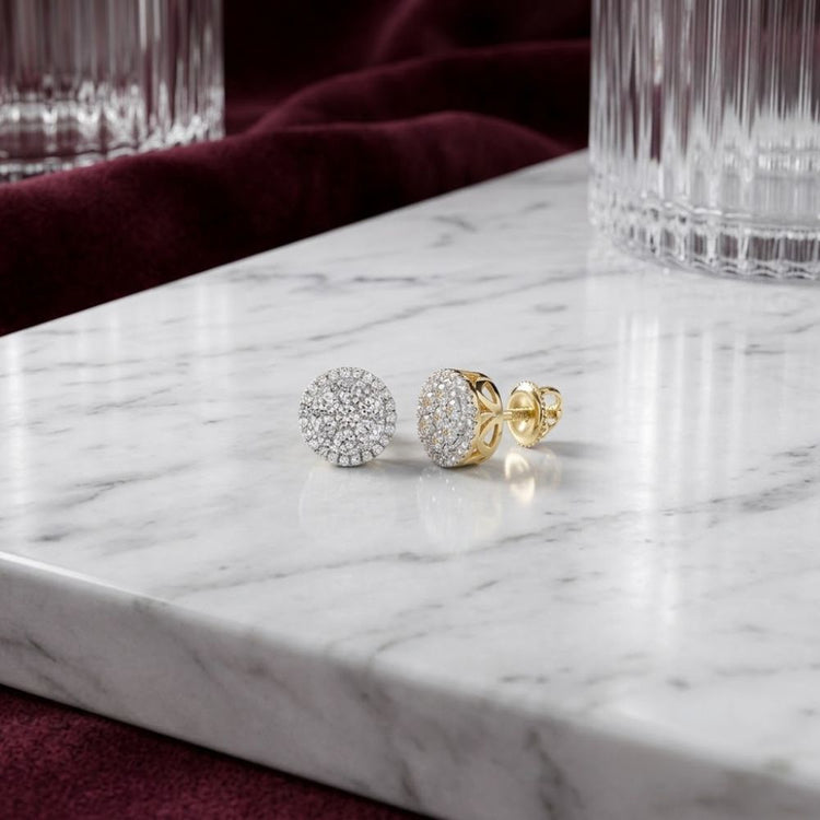 The 10k Yellow Gold Diamond Cluster Earrings 5/8 Cttw rest elegantly on a white marble surface, complemented by crystal glasses and a backdrop of burgundy fabric.