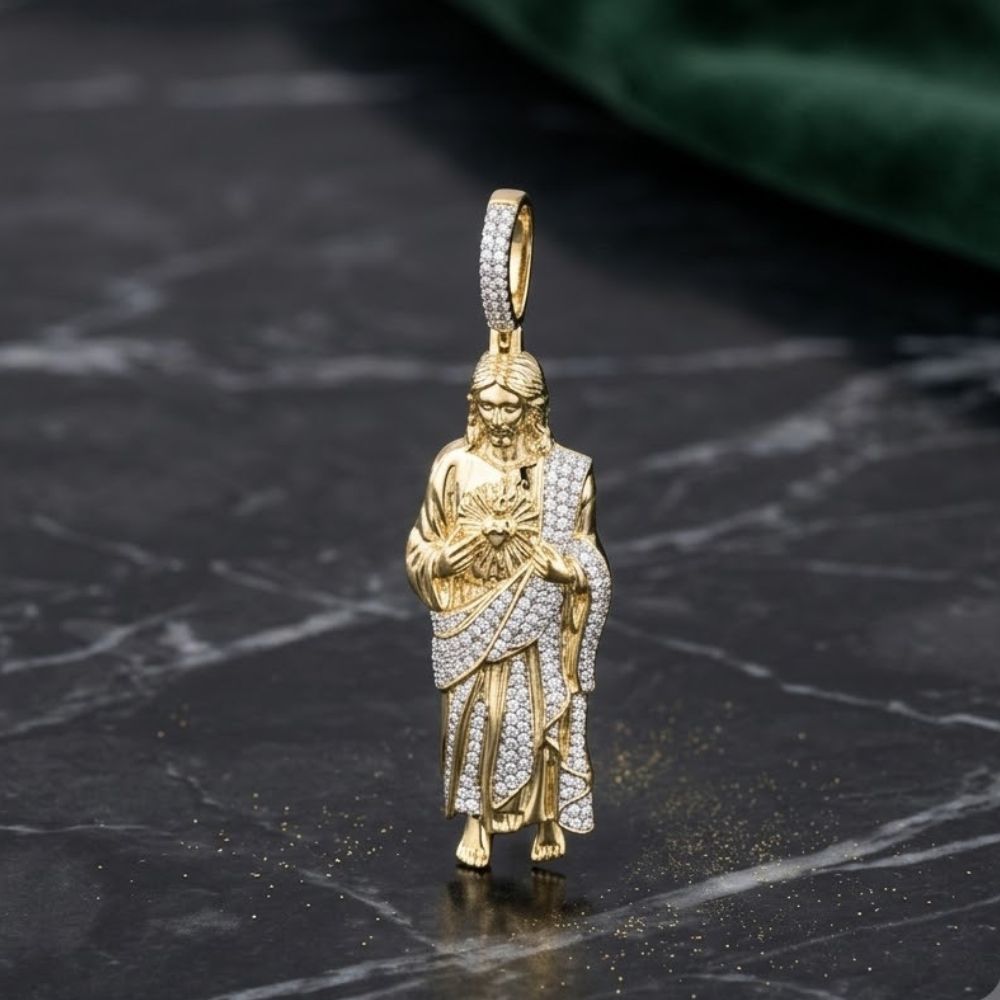 The 1CTW Natural Diamond Jesus Mens Charm in 10K gold rests on a dark marble surface, its robed figure with long hair and beard highlighted against a green fabric background.