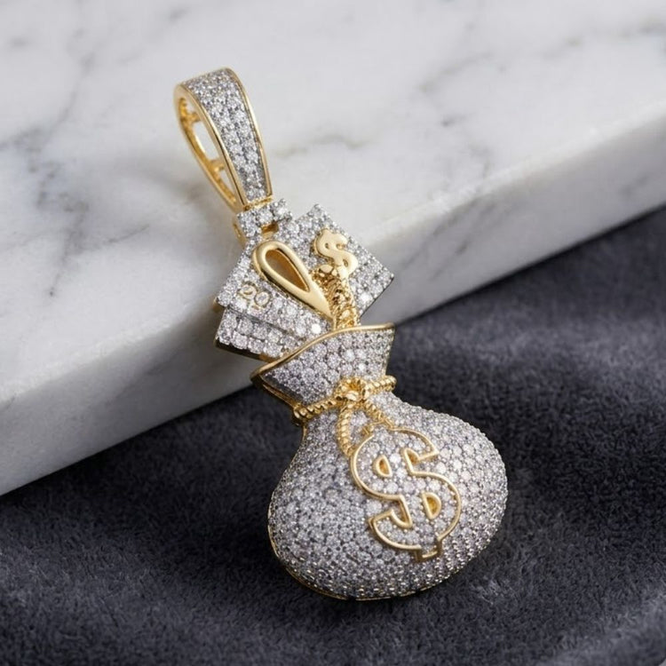 The 7/8CTW Natural Diamond Money Bag Dollar Men's Charm in 10K yellow gold sparkles with diamonds as it rests on a dark textured fabric beside a white marble surface.