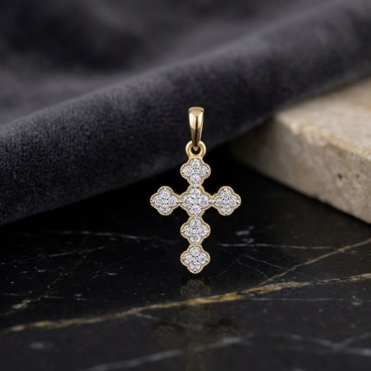 A 14K Gold 1/8 CTW Diamond Clover Cross Pendant, adorned with sparkling diamonds in an elegant clover design, rests gracefully on a sleek black marble surface, framed by a rolled dark gray fabric and a beige stone slab. This exquisite pendant radiates both timeless sophistication and contemporary style.