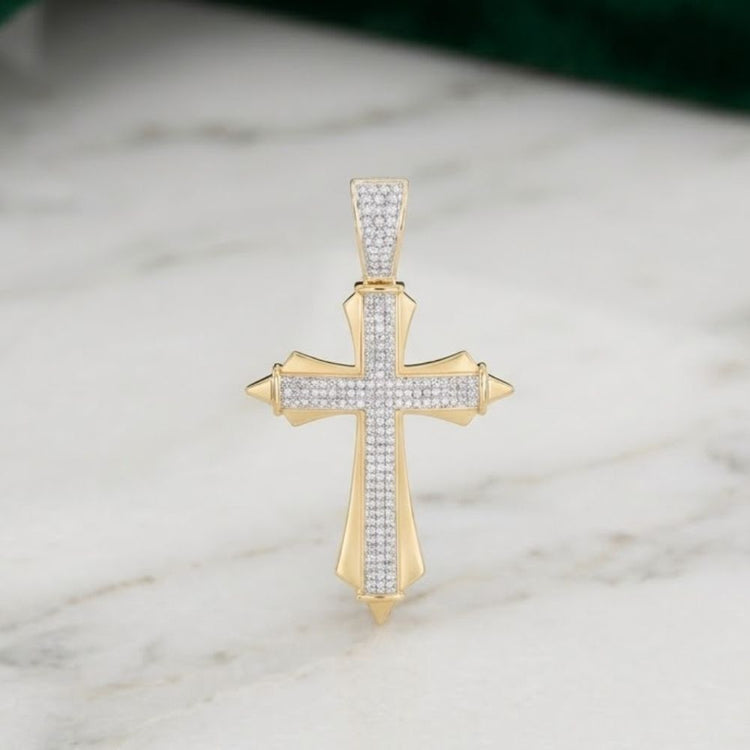 A 10K Yellow Gold Men's Diamond Cross Charm, totaling 5/8 CTW, featuring pointed tips and rows of small natural diamonds, stands upright on a white marble surface against a green background.