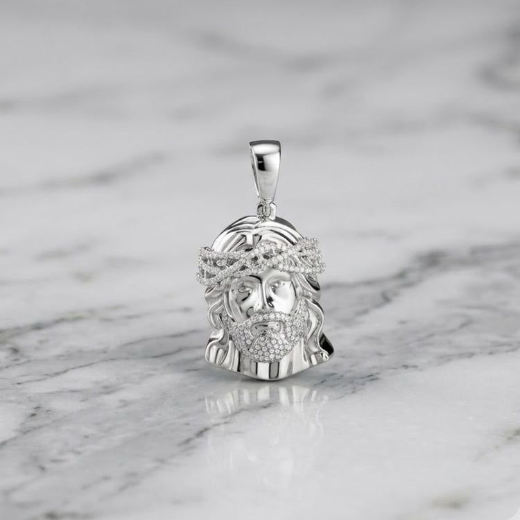 The Diamond Jesus Face Charm 3/4CT Sterling Silver, featuring a detailed bearded face with a crown of thorns design, rests on a white marble surface with gray veining, making it an ideal men's pendant.