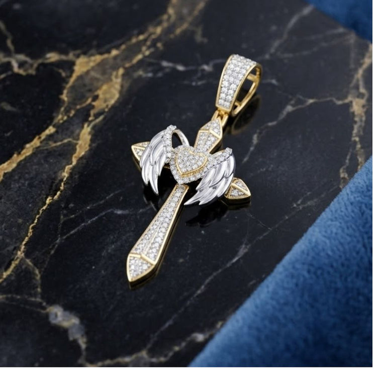 The 1 1/5CTW Natural Diamond Chrome Hearts Cross Charm in 10K gold, with angel wings and a heart at the center, is shown on black marble with gold veining and a blue textured edge—ideal for hip hop jewelry fans.