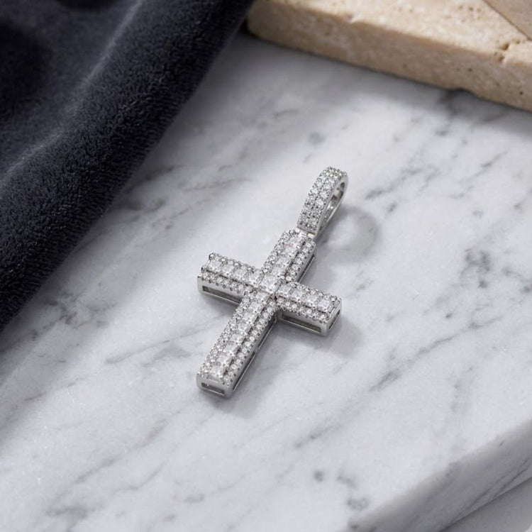 The Sterling Silver CZ Cross Religious Pendant, adorned with sparkling cubic-zirconia stones, is showcased on a white marble surface beside a black cloth and a beige stone, creating a striking display of religious jewelry.