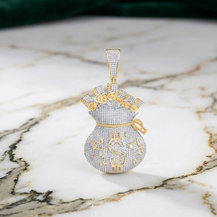 The 10k Gold Diamond Dollar Money Bag Charm 4.75CTW is a striking pendant shaped like a money bag, adorned with sparkling diamonds and gold accents. Featuring a prominent S and dollar signs, this charm rests elegantly on a marble surface with green fabric in the background.