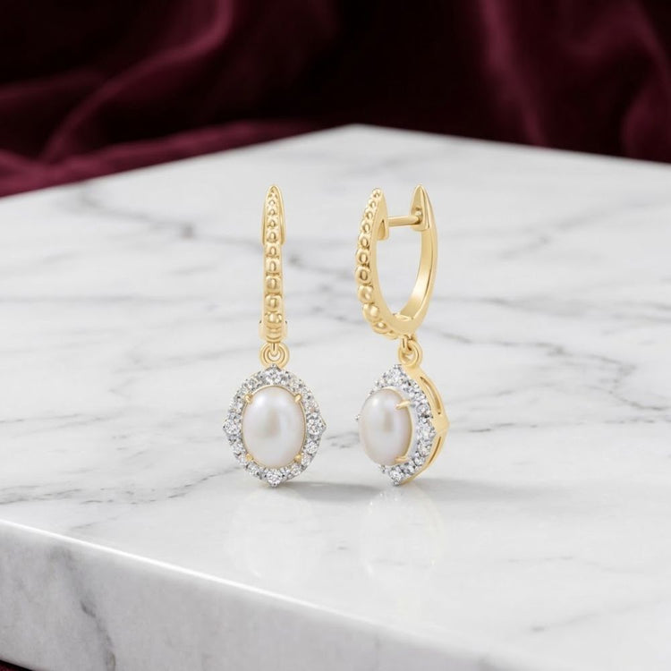 1/5 CTW Natural Diamond Opal Dangling Earrings in 10K yellow gold, showcasing elegant gold hoops with oval opals encircled by a sparkling halo of natural diamonds, presented on a white marble surface against a softly blurred burgundy fabric background.