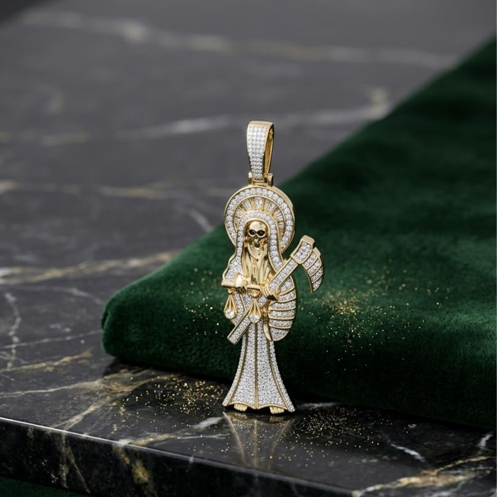 The 1-3/4CTW Natural Diamond Santa Muerte Charm in 10K gold features a skeletal figure with a halo and scythe, adorned with natural diamonds, and is displayed on dark green velvet atop a black marble tabletop.