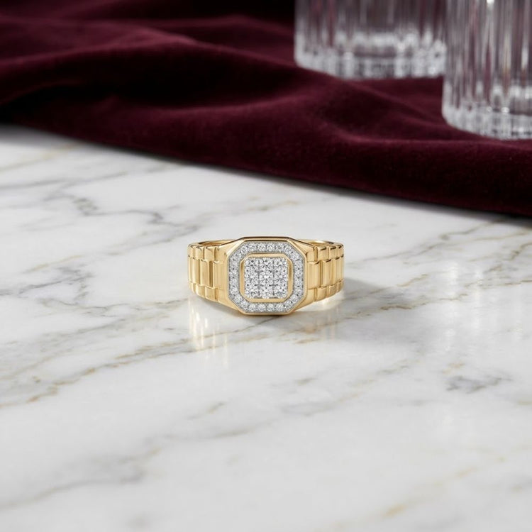 A 1/4CTW natural diamond men’s ring crafted in 10k yellow gold, featuring a square diamond cluster, rests on a white marble surface. In the background, a deep red velvet cloth and clear glass tumblers accentuate the refined elegance of this exquisite ring.