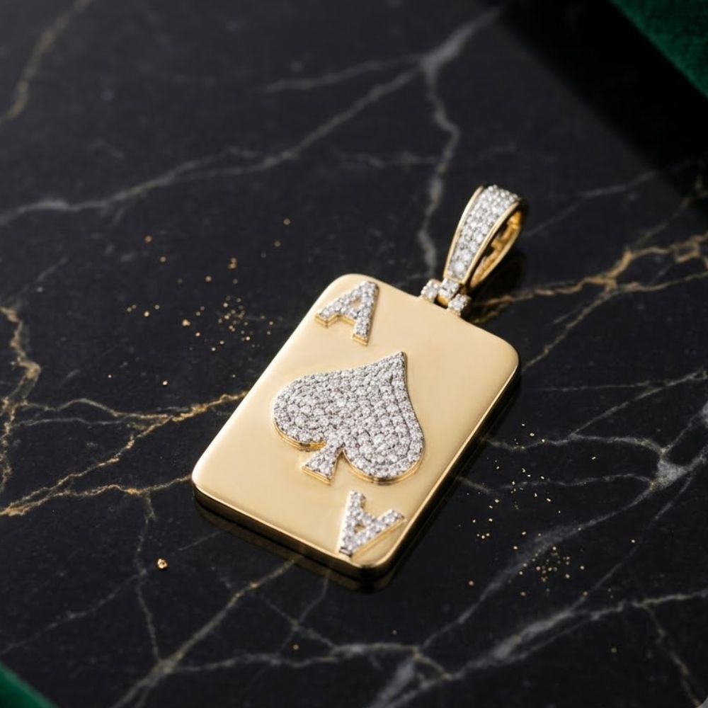 The Diamond ACE Charm 1/2CT 10K Yellow Gold features an ace of spades card design with natural diamond accents on the spade and A letters, displayed on a black marble surface with gold veining.
