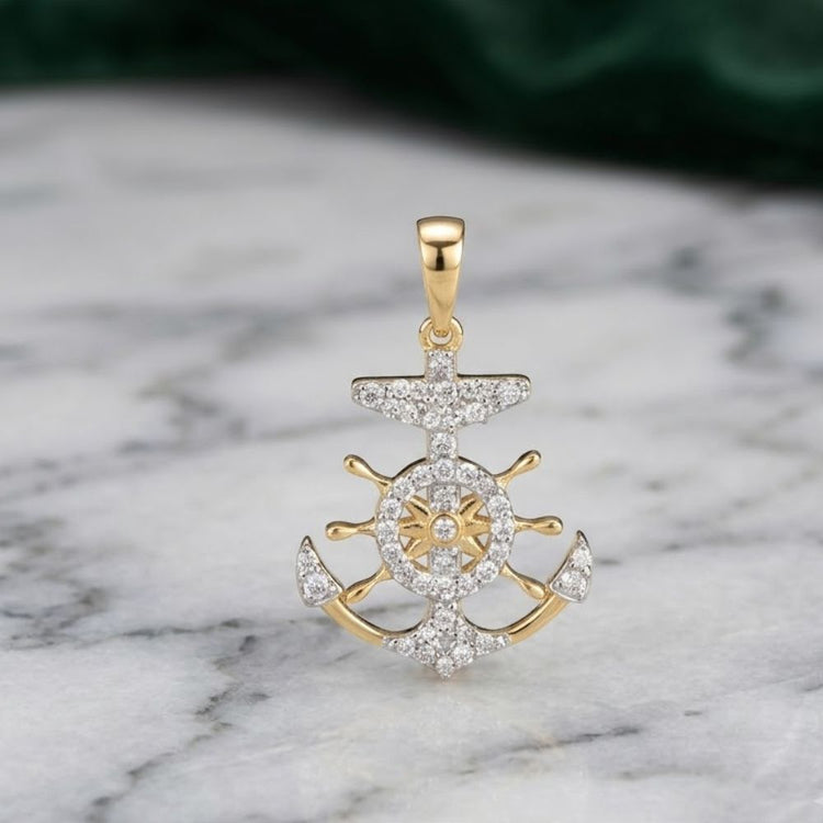 A 10k yellow gold anchor pendant, featuring a ship wheel design and adorned with 1/5 CTW sparkling diamonds, rests on a white marble surface with subtle gray veining.