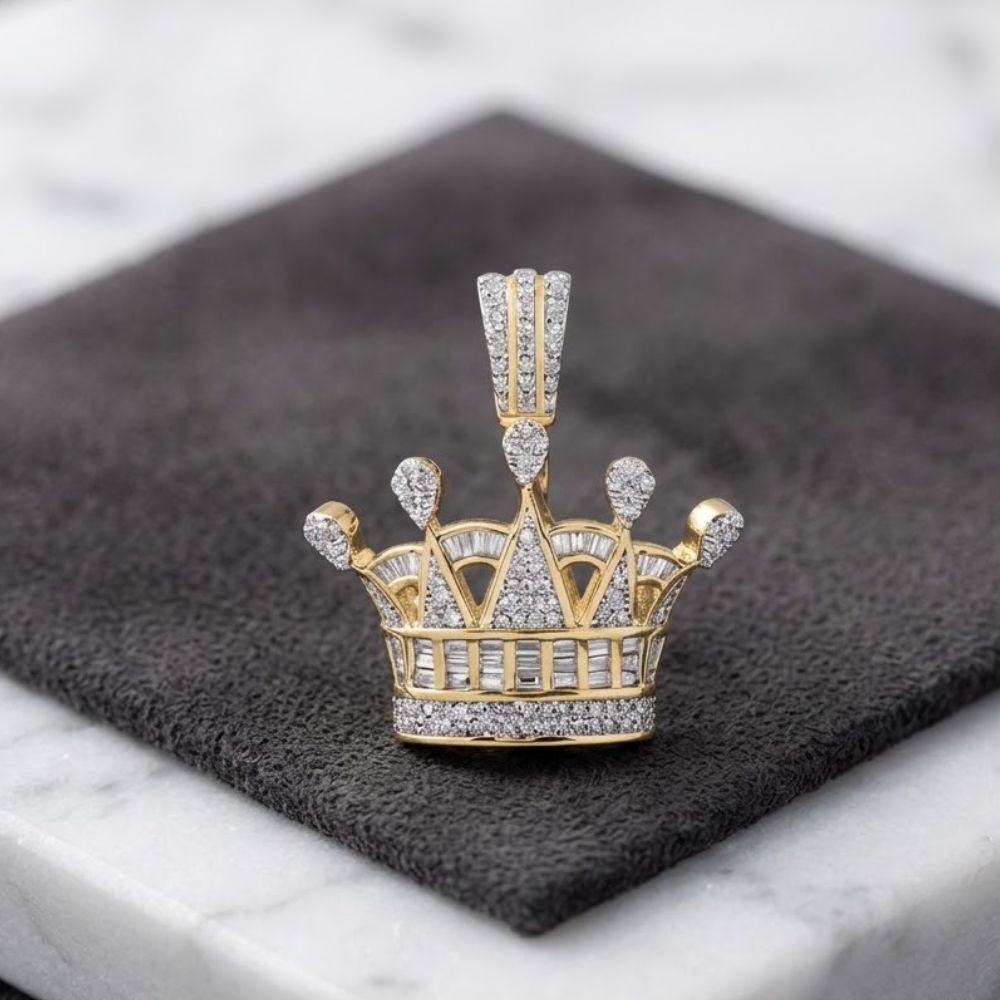 The Diamond Crown Pendant 7/8 CTTW 10K Gold, from Nicole’s Dream Collection, shines with diamond accents as it rests on a dark textured cloth over a white marble surface.