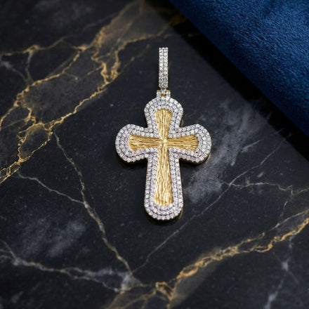 The 7/8CTW Natural Diamond Cross Mens Charm in 10K Gold rests on black marble with gold veining, while a touch of blue textured fabric at the edge highlights this striking natural diamond jewelry piece.