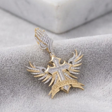 The Diamond Winged Cross Charm 1 7/8 CTTW Gold is a men's 10K yellow gold and diamond pendant with praying hands above a cross, angel wings, and a "GODSPEED" banner. It is shown resting on gray fabric.