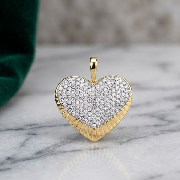 A 10K yellow gold diamond heart pendant, featuring a center encrusted with small natural diamonds (1 1/5 cttw), is elegantly displayed on a marble surface near a dark green fabric. The 10K Yellow Gold Diamond Heart Pendant beautifully captures timeless romance and refined style.