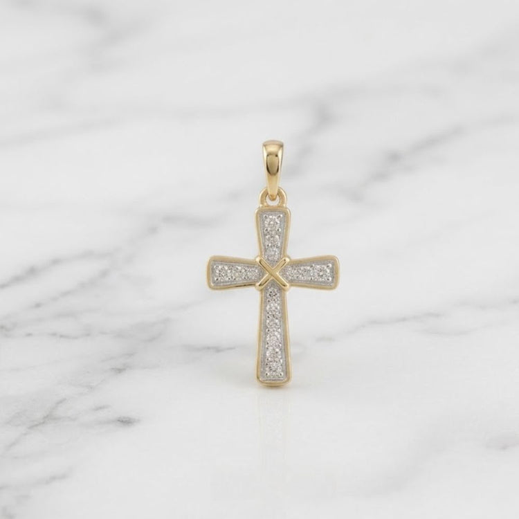 The 10K Yellow Gold 1/6 CTW Diamond Cross Pendant rests on a white marble surface with gray veining.