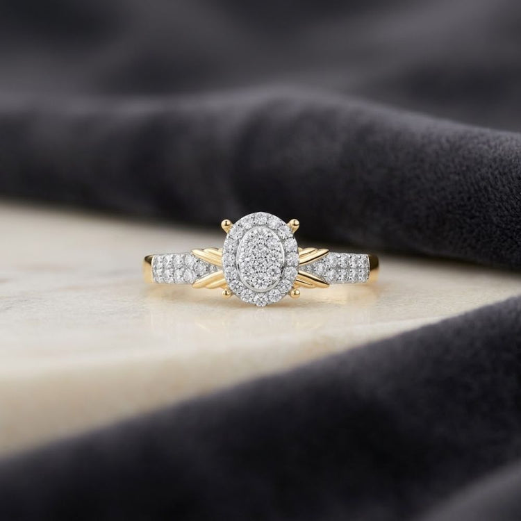 Introducing the 1/4CTW Diamond Oval Halo Engagement Ring in 10K Gold, a breathtaking piece that boasts a captivating cluster of natural diamonds at its center, beautifully embraced by a sparkling oval halo and accent stones. The diamond-studded band enhances its brilliance, while its elegant display on marble with a dark fabric backdrop emphasizes the ring’s timeless sophistication and refined beauty.