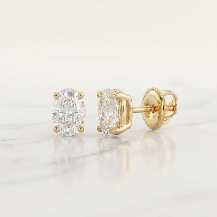 14k Gold Natural Diamond Oval Stud Earrings 1/5 CTW are displayed on a white marble surface; one earring stands upright, while the other lies on its side to show the backing.