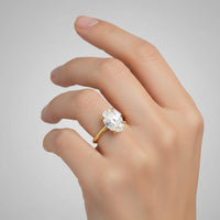 A hand with neatly manicured nails wears a 1.72ct oval-cut lab diamond engagement ring in 14k solid yellow gold on the ring finger against a plain gray background.