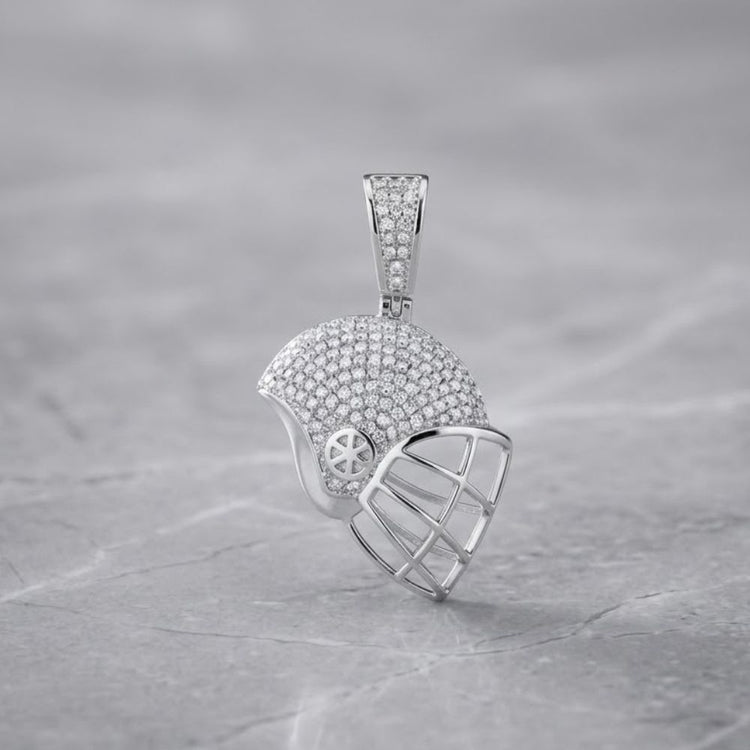 The Sterling Silver Diamond Helmet Pendant 3/4 CTW, crafted in the shape of a baseball catcher's mask and encrusted with shimmering diamonds, captures the bold style of sports helmet pendants. Displayed on a smooth, light gray marble surface, this piece highlights the elegance and brilliance of round diamond jewelry.