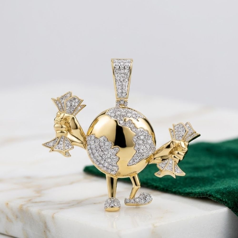 The 1CTW Diamond Men’s Globe Charm in 10k gold features a cartoon globe with arms and legs, holding diamond-encrusted cash, shown gleaming atop marble beside a green cloth.