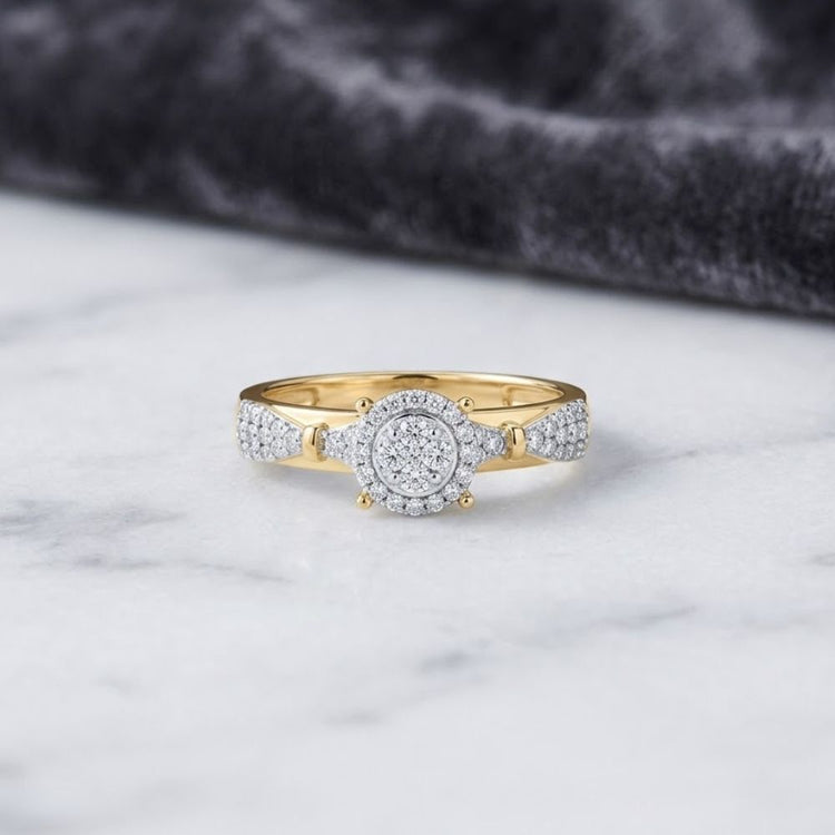 The 1/3CTW Diamond Round Single Halo Engagement Ring in 10k gold features a stunning cluster of round diamonds at its center, surrounded by a halo and accented by additional diamonds along the band. Presented on a white marble surface with a gray velvet cloth in the background, this elegant ring exudes timeless sophistication.