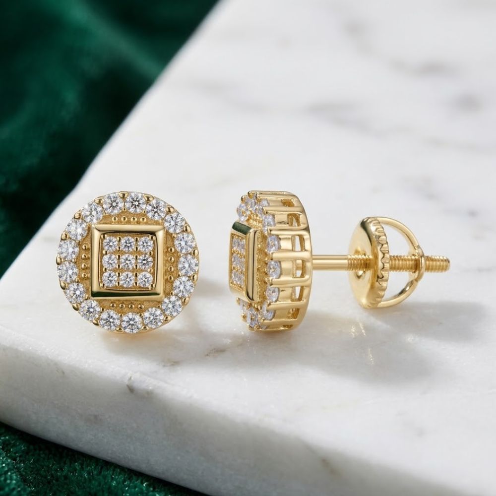 The Yellow Tone Moissanite Stud Earrings 0.84ct Silver feature a circular design and sparkling stones, displayed on white marble with a green fabric background.