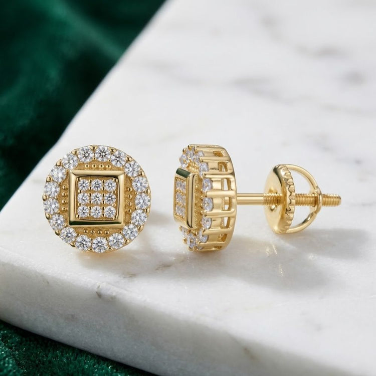 The Yellow Tone Moissanite Stud Earrings 0.84ct Silver feature a circular design and sparkling stones, displayed on white marble with a green fabric background.