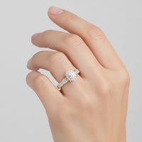 A hand with neatly manicured nails wears the 1/4CTW Diamond Oval Halo Engagement Ring in 10K gold, featuring a prominent oval diamond center surrounded by a glittering halo of smaller diamonds and additional diamonds adorning the band, set against a plain light background.