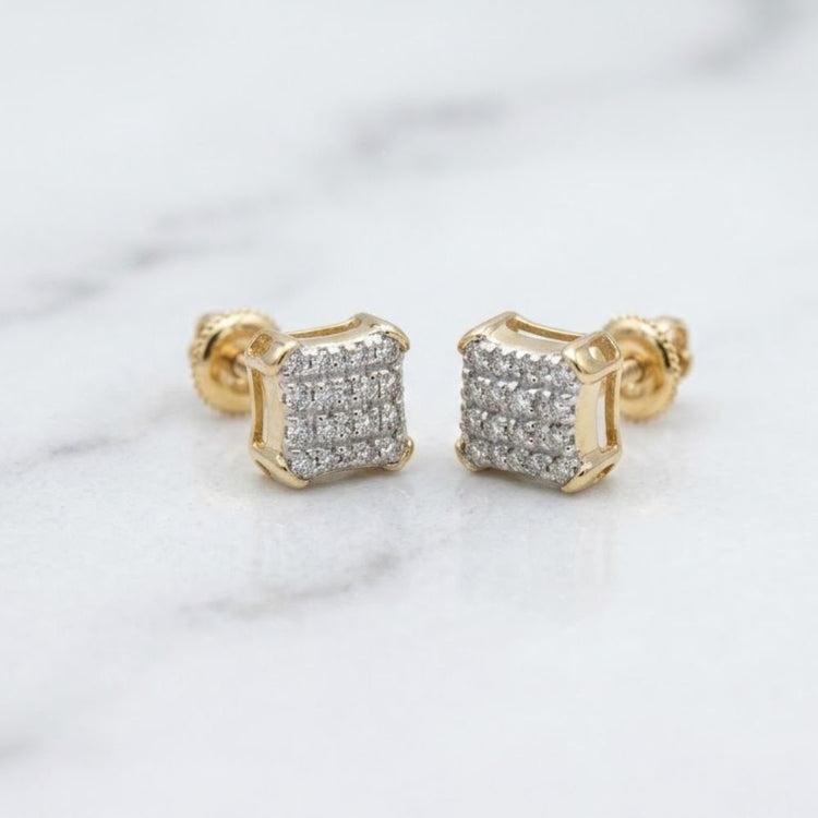A pair of 10K Gold Diamond Square Earrings 1/10 CTTW featuring square-shaped fronts encrusted with small, sparkling diamonds, displayed on a white marble surface.