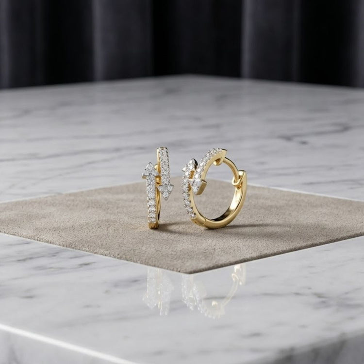 A pair of 1/4 CTW Natural Diamond Fashion Hoop Earrings in 10K gold is displayed on a square beige mat, set atop a white marble surface with a dark, softly blurred background. These elegant earrings effortlessly combine timeless style and modern sophistication.