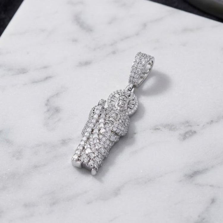 The Silver Baguette Moissanite St. Jude Pendant, expertly crafted from 925 sterling silver and adorned with brilliant baguette-cut moissanite stones, features a robed religious figure with a luminous halo and is displayed gracefully atop a white marble surface.