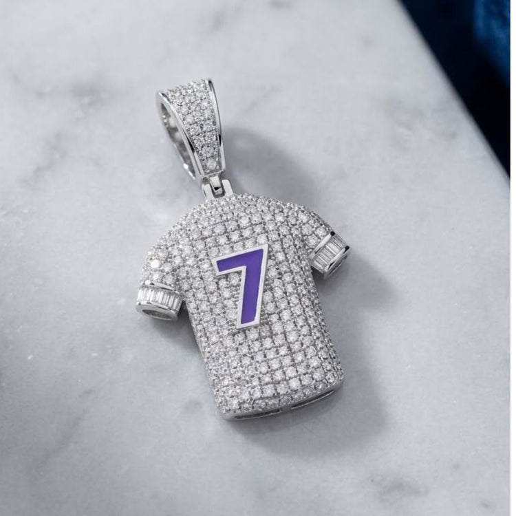 Showcasing a bold hip-hop aesthetic, the Sterling Silver Diamond Number 7 Jersey Charm 1.25 CTW features a jersey-shaped pendant encrusted with diamonds and highlighted by a striking purple number 7 on the front. Photographed on a marble surface, this eye-catching charm is a standout addition to any jewelry collection.